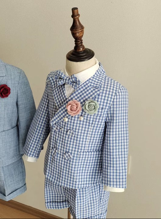 Detailed close-up of the blue gingham boy wedding outfit, featuring a double-breasted blazer, bow tie, and blush and green floral pin accents.