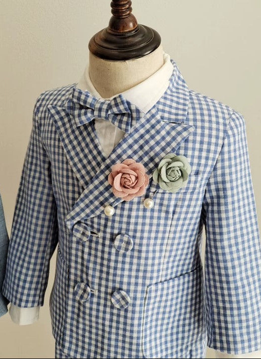 Detailed close-up of the blue gingham boy wedding outfit, featuring a double-breasted blazer, bow tie, and blush and green floral pin accents.