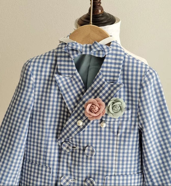 Detailed view of the blue gingham boy wedding blazer featuring a double-breasted design, bow tie, and blush and green floral pins. Perfect for formal occasions.
