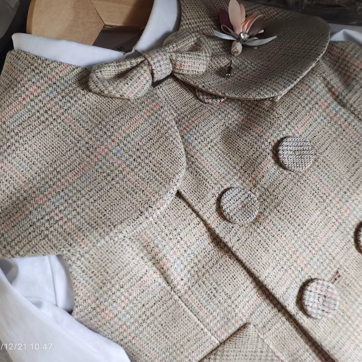 Close-up view of vintage baby boy wedding suit in beige houndstooth fabric, featuring double-breasted buttons, cape, and bow tie. Elegant page boy outfit.