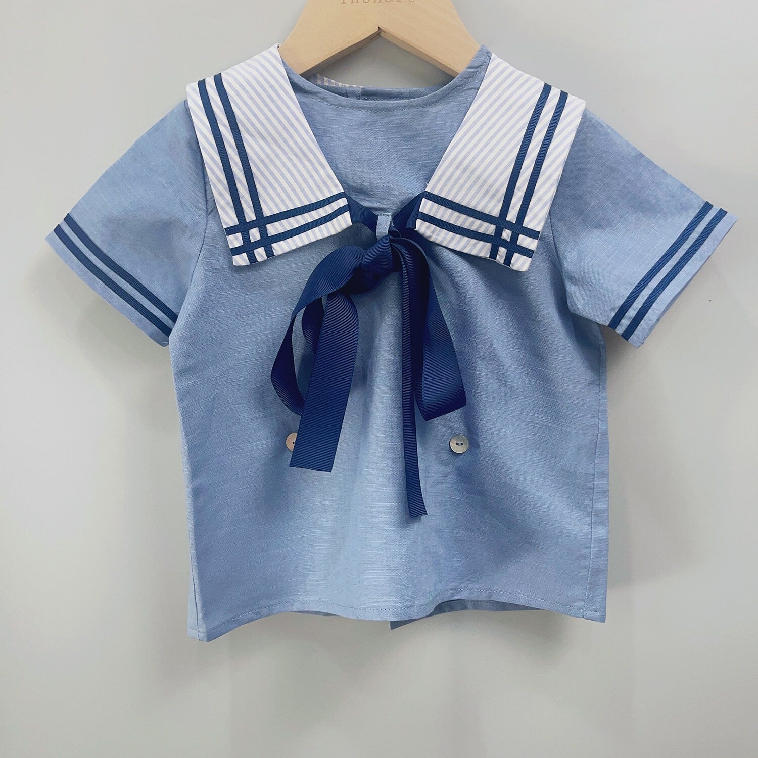 Front view of classic sailor-style boys' shirt with a nautical collar, navy ribbon tie, and light blue fabric, perfect for special occasions like christenings and birthdays for boys aged 12 months to 6 years.